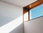 A window through which a beam of light enters a room, hitting a white wall.