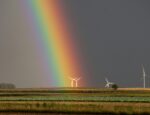 A rainbow over a field with four wind turbines.