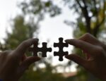 A person holding up two puzzle pieces to the sky.