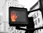 A hand signaling do not cross on a cross walk sign.