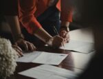 Two people signing documents on a table.