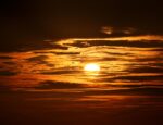 A sun behind clouds, projecting an orange hue to the sky.