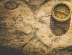 A compass laying on a yellowed world map.