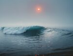 An ocean wave with the moon in the sky, which is foggy.