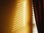 Light shining through a window with curtains and blinds.